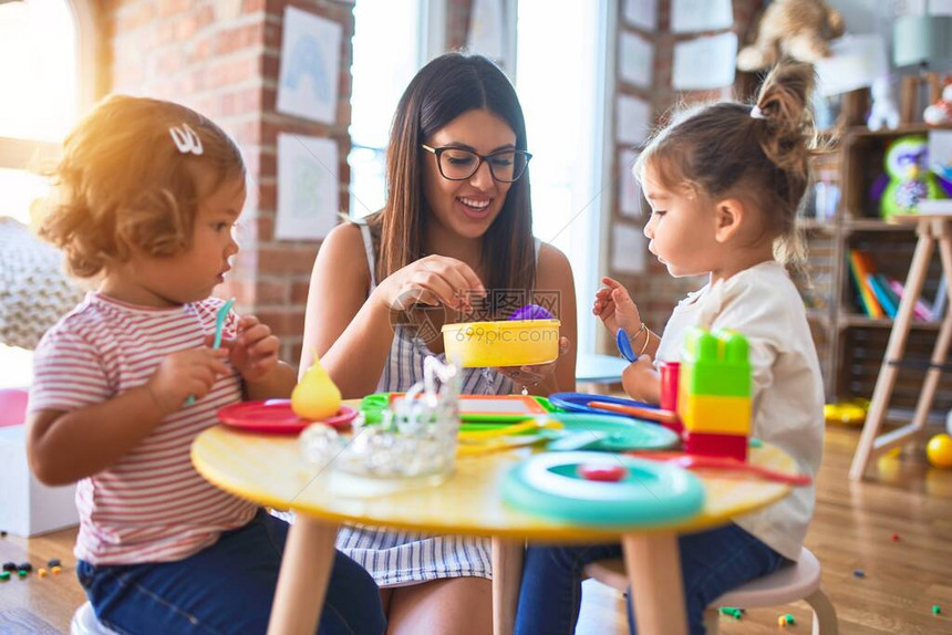 年轻漂亮的老师和幼儿在幼儿园用塑料食品和图片