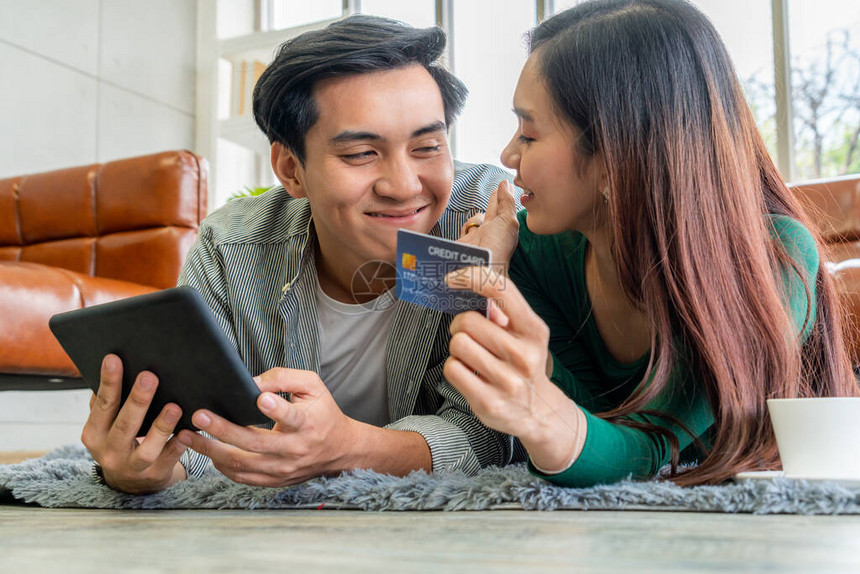 年轻夫妇在家中使用信卡在互联网站上进行在线购物信用卡上的号码是模拟的信用卡上没有显示个人信息在线图片