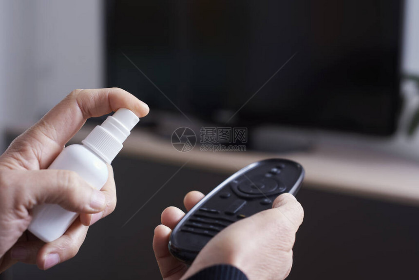 一个白人男子通过从白瓶中喷洒消毒剂对电视机遥控器进图片