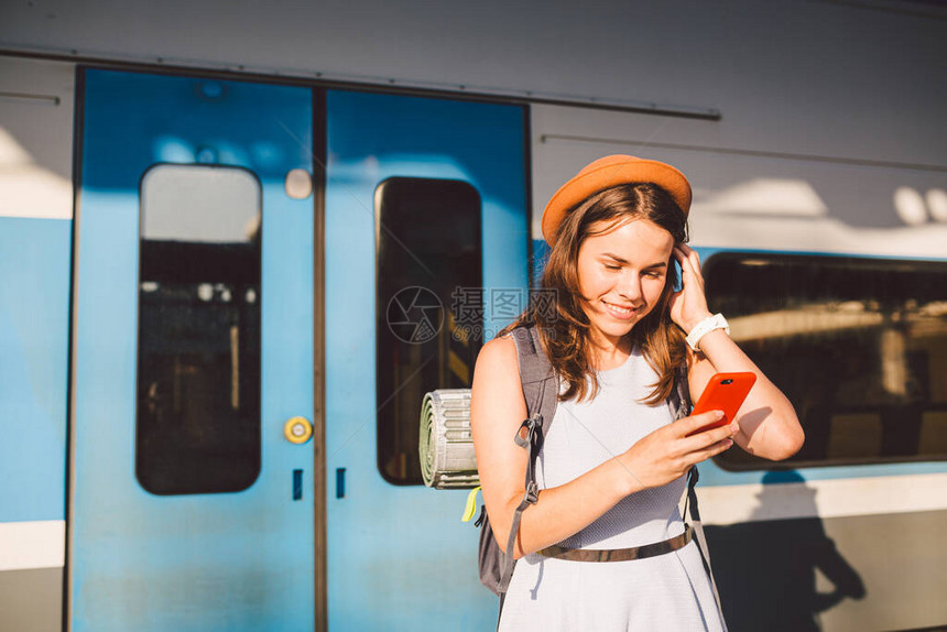 铁路主题美丽的年轻女子背着包站在台上的铁路列车附近使用手机图片