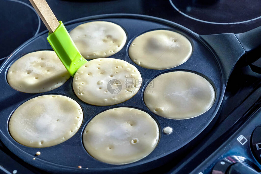 煎饼锅带微笑脸煎饼在厨房的炊具上烹饪图片