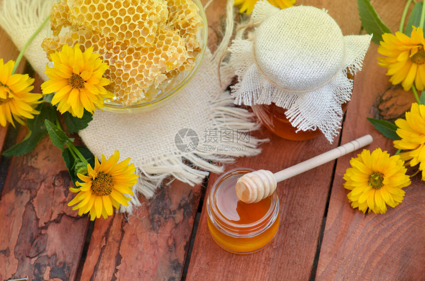 蜂蜜的罐子有鲜花背景的木桌上的蜜蜂窝图片
