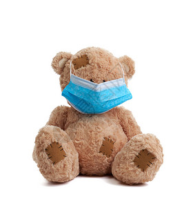 大泰迪熊坐在白色背景的蓝色医用口罩中图片