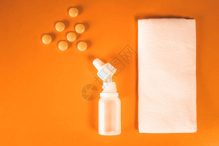 橙色背景上带有片剂和纸手帕的白色塑料鼻喷雾剂背景图片