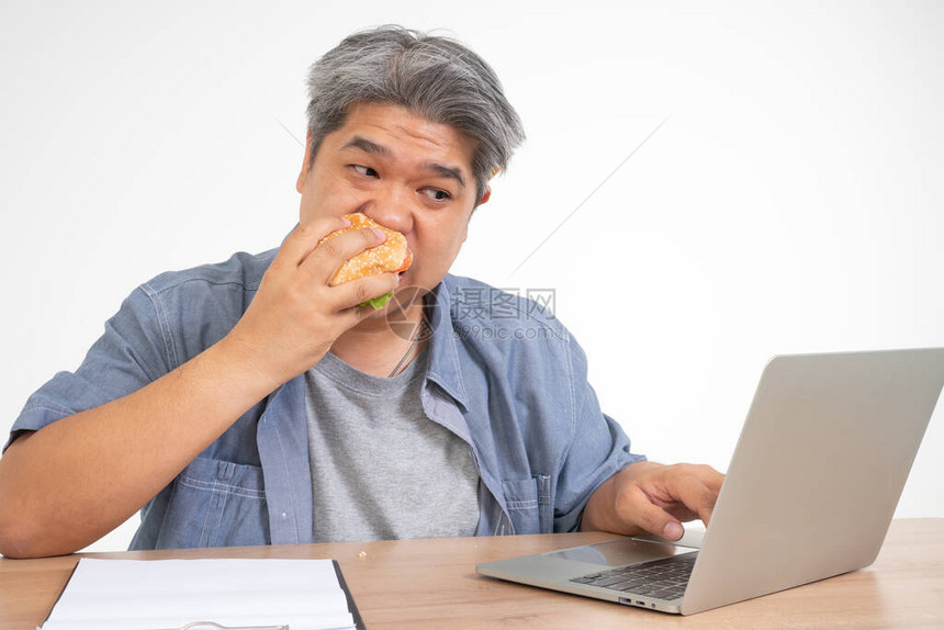 亚洲人在办公桌上工作和吃汉堡一个忙碌的商人的概念不能工作左平衡和不照顾健康图片