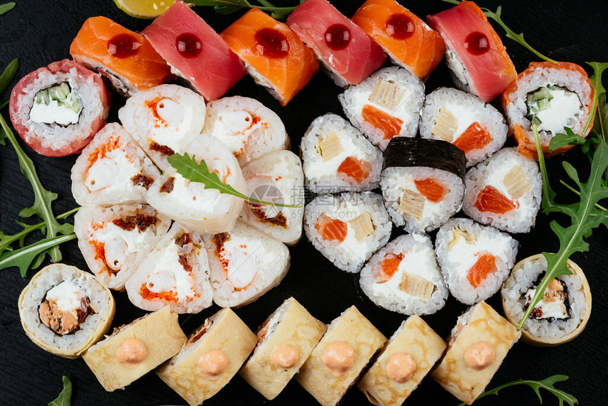 一套寿司卷配有鲑鱼虾和熏鱼黑盘上图片