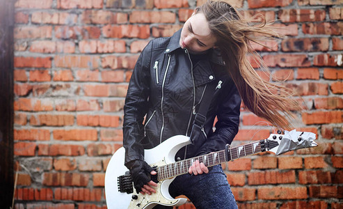 美丽的年轻女孩摇杆与电吉他一个穿着皮夹克的摇滚音乐家女孩拿着吉他摇滚乐队独奏者弹吉他背景图片