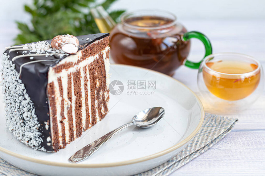 一片带有巧克力糖衣的斑马蛋糕在浅色背景上背景是一个装有花茶的杯图片