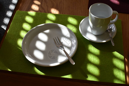 在一张桌子上放着咖啡和蛋糕一个带叉子的蛋糕盘一个杯子和碟子图片