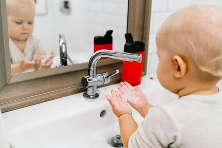 儿童独立地用一种特殊的消毒剂将自己的手洗到一个明亮的浴室里图片