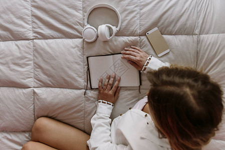 白人拉丁语白种人金发女孩坐在床上自由职业者在家工作与手机记事本图片