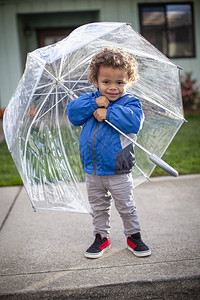 可爱的小男孩在下雨天离开家外出时打着伞图片
