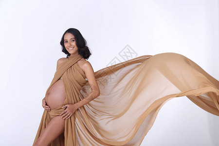 怀孕的亚洲印度晒黑皮肤女棕色金织物在空气中飘扬的肖像图片