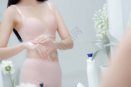 美丽感的年轻亚洲女照镜子在手上涂抹奶油和信息图片