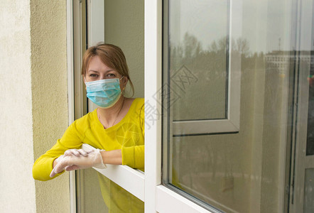 这名戴着防护口罩和手套的妇女站在公寓敞开的窗户前图片