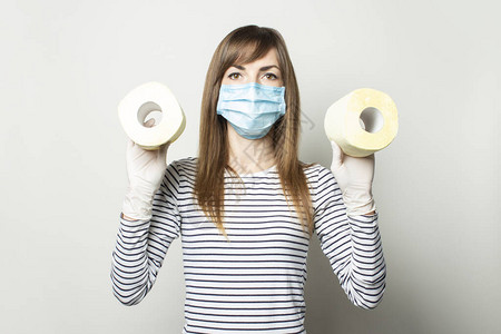 身戴医疗面具和手套的年轻女孩带着一卷轻背景的卫生纸图片