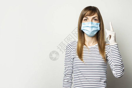 戴着防护医用口罩和乳胶手套的年轻女子将手指向一个明亮的孤立背景图片