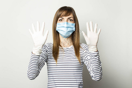 戴着防护医用口罩和乳胶手套的年轻女子在浅色孤立的背景下举手图片