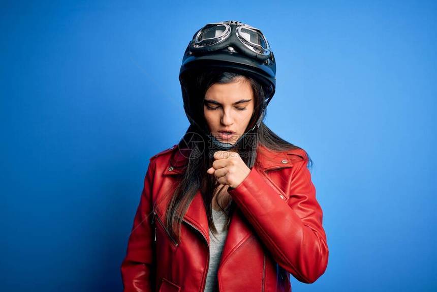 年轻漂亮的黑发摩托车手女人戴着摩托车头盔和夹克感觉不适和咳嗽作为感冒或支气管炎的症图片