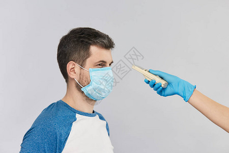 身穿蓝色衬衫和面部防护面罩的男子看着医生戴着蓝色手套的电子温度计图片