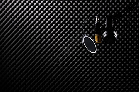 带过滤耳机杯的麦克风悬挂在黑暗音频工作室的吸音墙房间图片