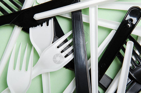 绿色背景上的塑料白色和黑色叉子和刀子图片