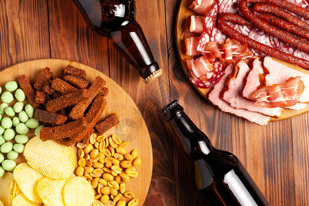 两瓶啤酒和各种零食每种品味都是木制背景的肉类产品香肠切片薯条图片