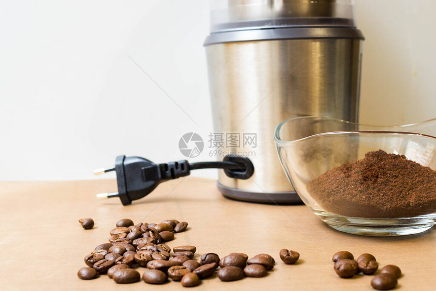 在家磨咖啡电动金属咖啡研磨机烤咖啡豆和米色桌子上的玻璃碗里的咖啡粉图片