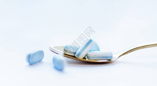 蓝药片在白色背景的金汤匙里药剂学概念图片