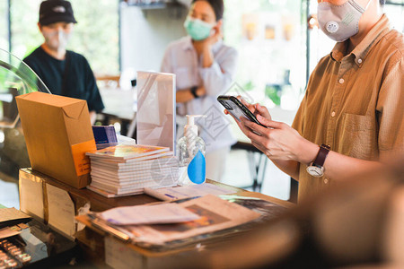 戴保护面罩在咖啡厅柜台用手机下图片