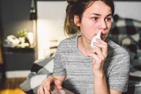 主题是季节感冒流鼻涕流感感染在家卧室床上的年轻白种女人在她的鼻子里喷药滴鼻涕过敏背景图片