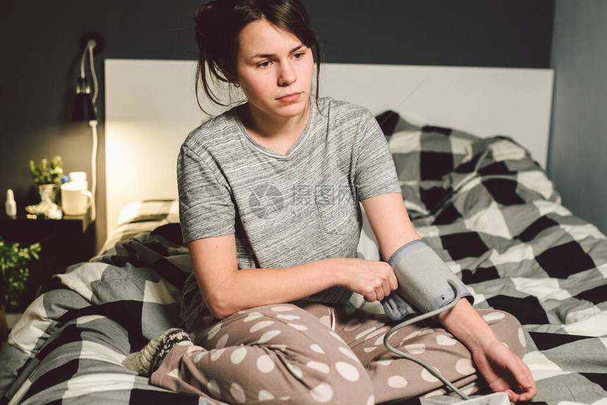 题目高血压高血压病22岁的年轻白种人妇女使用自动眼压计她把袖口放在胳膊上检查压力回家在卧室的床图片
