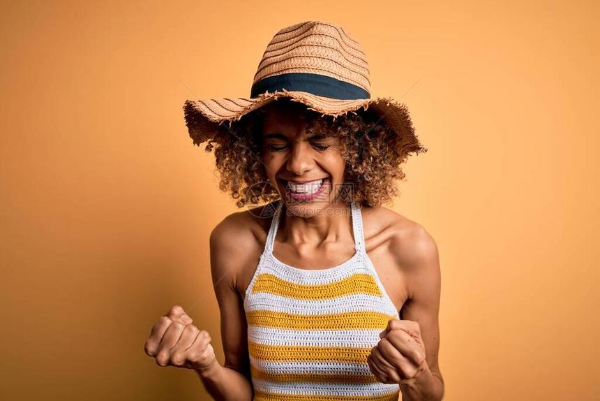 穿着暑假帽子和T恤的非洲美籍旅游女客非常快乐兴奋地以举起手臂微笑和为成功而尖叫来做赢家姿态庆祝概念图片