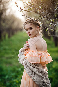 在开花的园里穿着轻便连衣裙的金发女孩女春季时尚的概念穿着漂亮裙子和针织毛衣的女孩在梨花背景图片