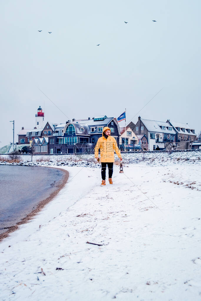 穿着黄雨夹克的青年男子在荷兰乌尔克灯塔附近的雪沙滩上行走图片