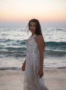 美丽的黑发女人的浪漫肖像穿着白色蕾丝裙的女人站在海边沙滩和日图片
