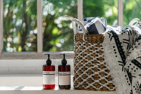 柳条篮中的大毛巾站在明亮浴室缸顶部的两瓶身体护理化妆品附近图片