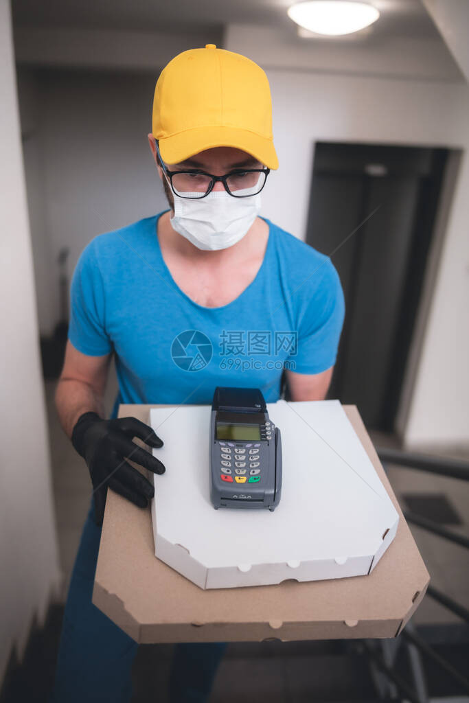 带防护医用口罩的送货员拿着披萨盒和POS无线终端图片