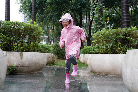 身穿粉红色雨靴和在水坑里跳水时行走图片