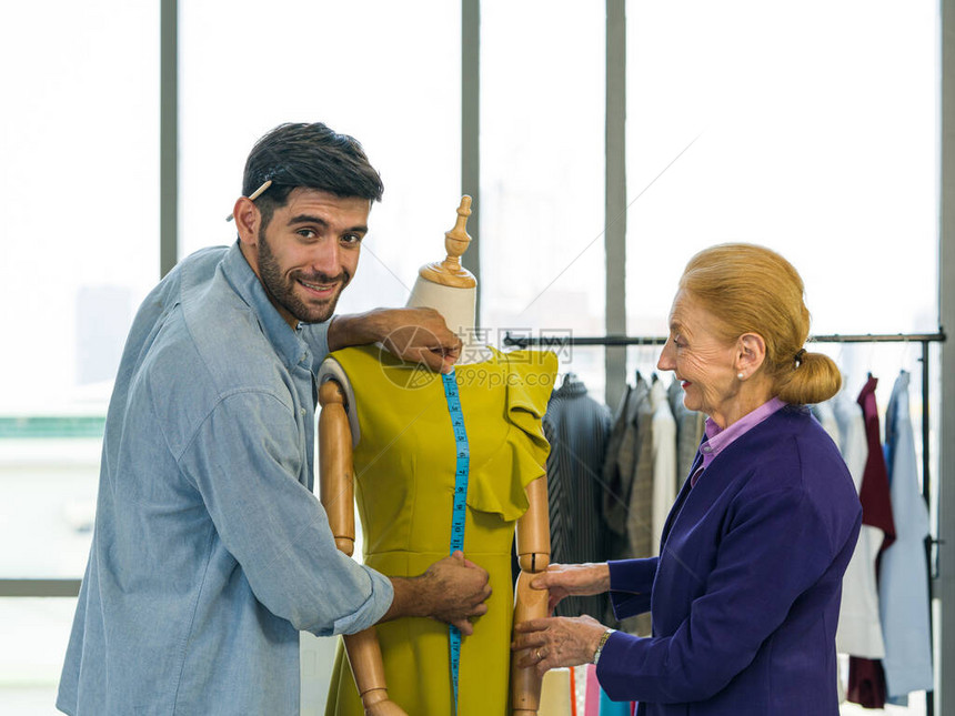 男人和女人在家庭基地布设计业务工作男裁缝从人体模型上测量从脖子到腰部的绿色连衣裙的长度老年顾客正在焦图片