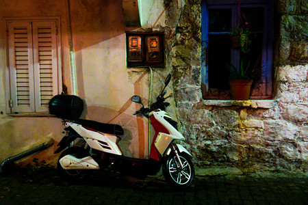 滑板车靠在墙上的夜间照片摩托车在希腊房子墙上的蓝色窗户在图片