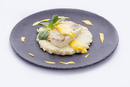 烤鳕鱼片放在意大利调味饭调味酱和康乃馨床上图片