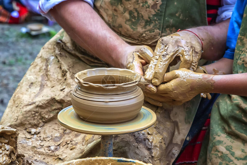 一名陶艺大师教一个想学习如何雕塑罐子的孩子图片