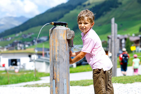 小学生男孩在炎热的夏日玩水泵背景上的奥地利山脉儿图片
