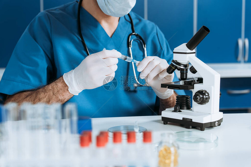 医学面具和乳胶手套中生物学家在显微镜附近携带注图片