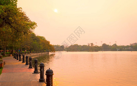 夏日傍晚的湖边公园日落阳光照亮的花园小径公园车道风景场中的红色和橙色太阳落山达库里亚湖镇加尔各答西孟加拉邦印度背景