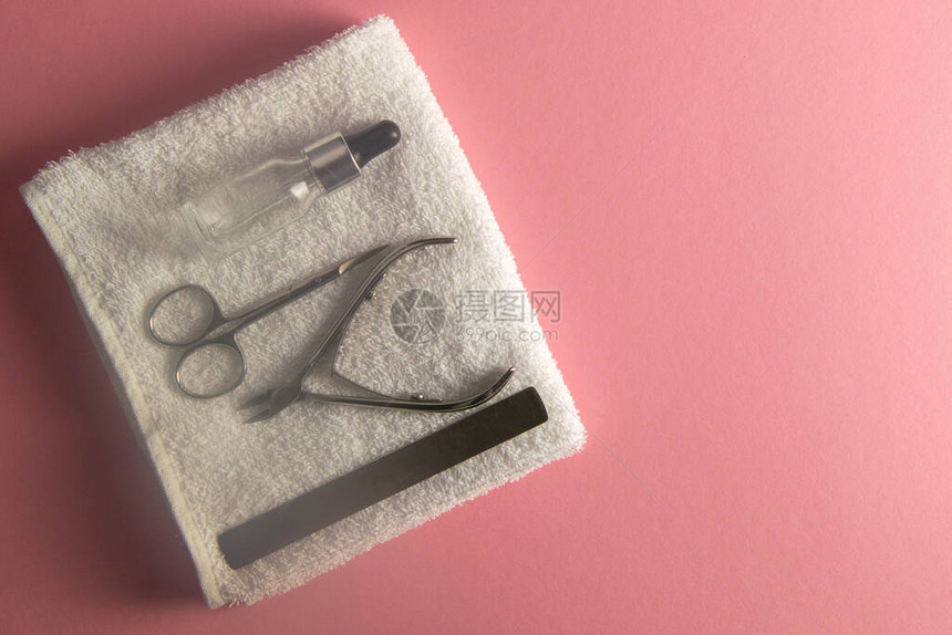 指甲锯角质层剪指甲剪和手油站在粉红色背景上的白色毛巾上具有清晰图片