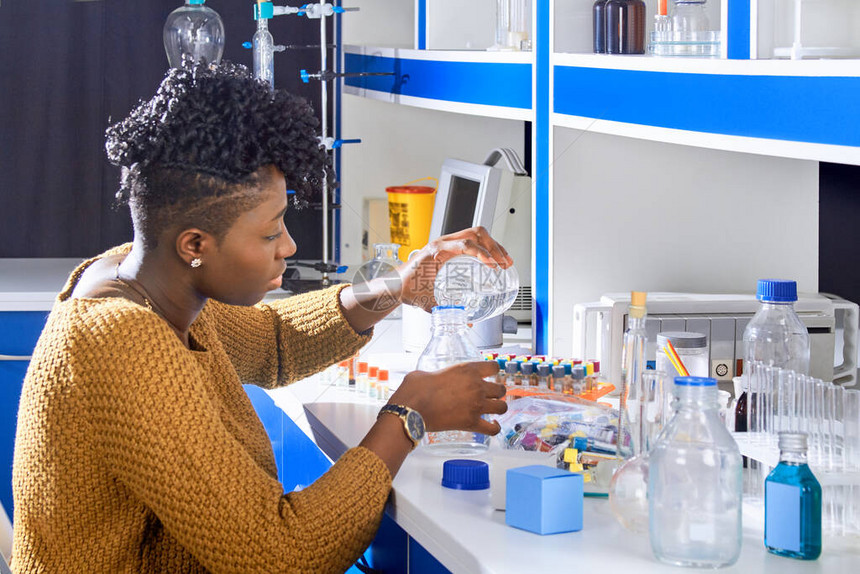 年轻的非洲女技术人员或科学家正在将缓冲溶液从一个瓶子倒入另一个瓶子图片