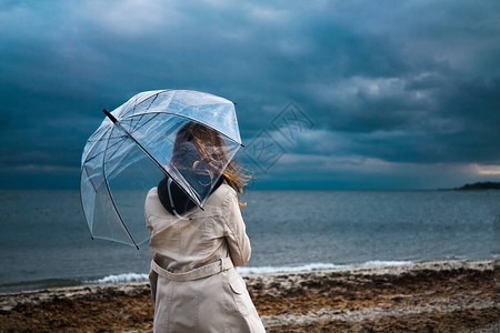 女孩在多云的天气里拿着透明的雨伞沿着海边的海滩散步雷暴和大雨下雨图片