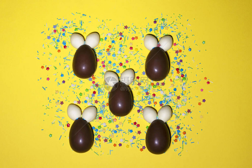 由含甜色粉末的巧克力制成的兔子躺在明亮黄色背景上图片